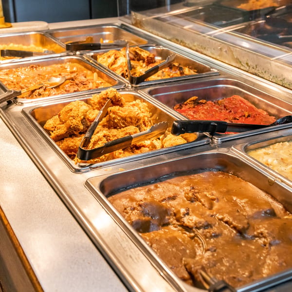 A buffet line with various hot dishes, including fried chicken, mashed potatoes, and gravy.