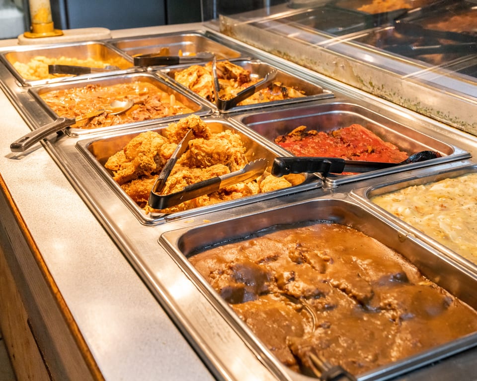 A buffet line with various hot dishes, including fried chicken, mashed potatoes, and gravy.