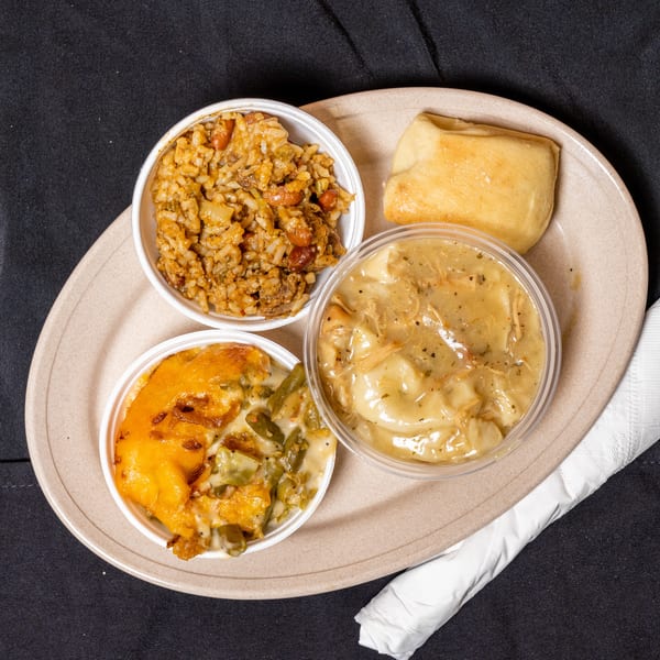 A takeout meal with jambalaya, chicken and dumplings, green bean casserole, and a roll.
