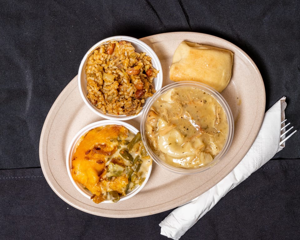 A takeout meal with jambalaya, chicken and dumplings, green bean casserole, and a roll.