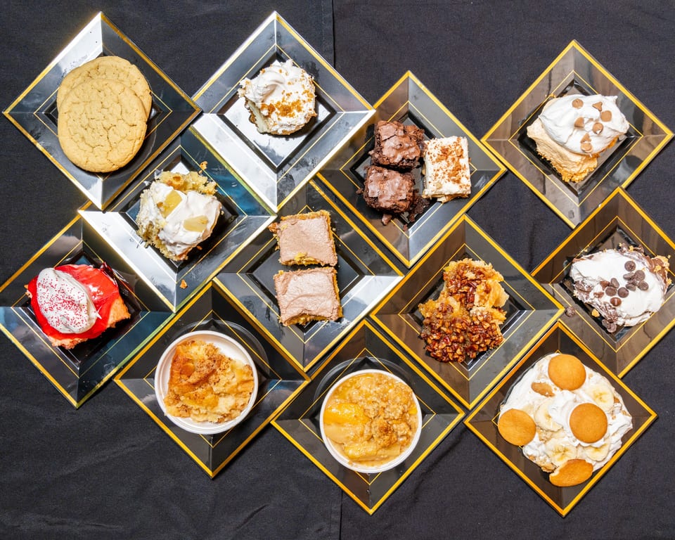 An overhead view of various desserts, including cookies, brownies, cakes, and fruit crisps, on black and gold plates.