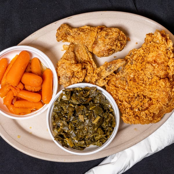 Fried chicken pieces, a side of glazed carrots, and collard greens on a plate.