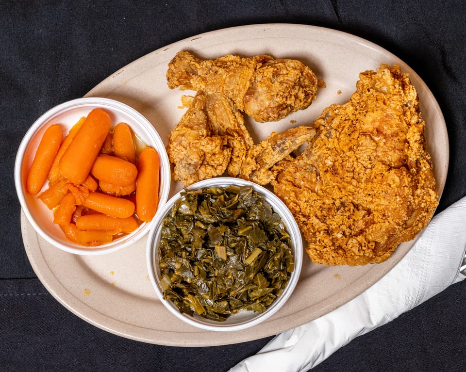 Fried chicken pieces, a side of glazed carrots, and collard greens on a plate.