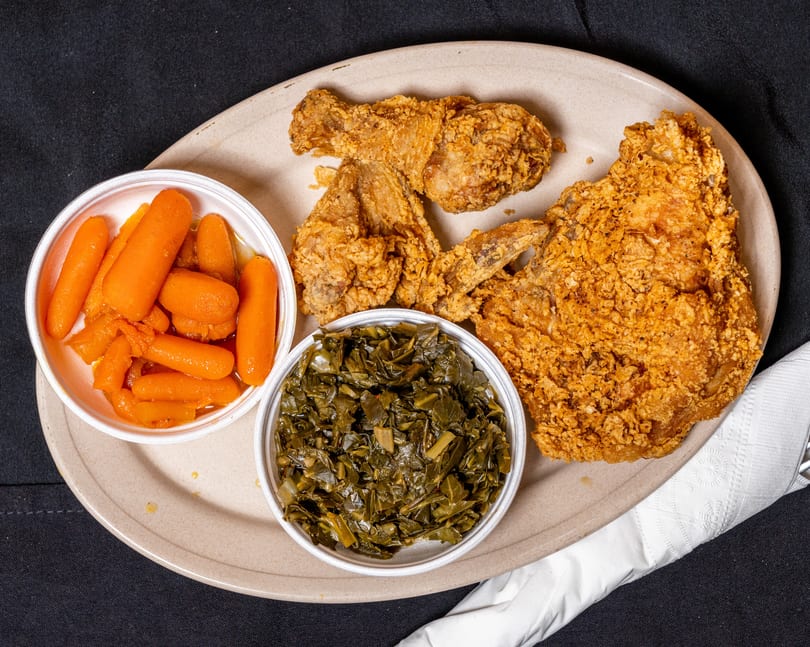 Fried chicken pieces, a side of glazed carrots, and collard greens on a plate.