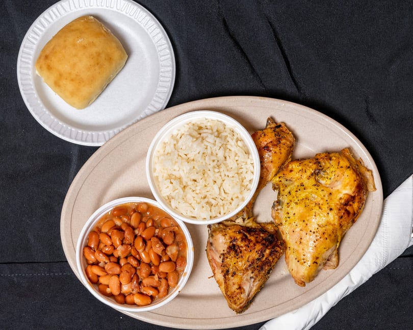 Grilled chicken with rice and beans, served with a dinner roll on a black tablecloth.