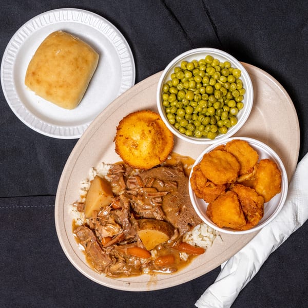 Pot roast with rice, potatoes, carrots, corn muffin, peas, and fried okra on a plate.