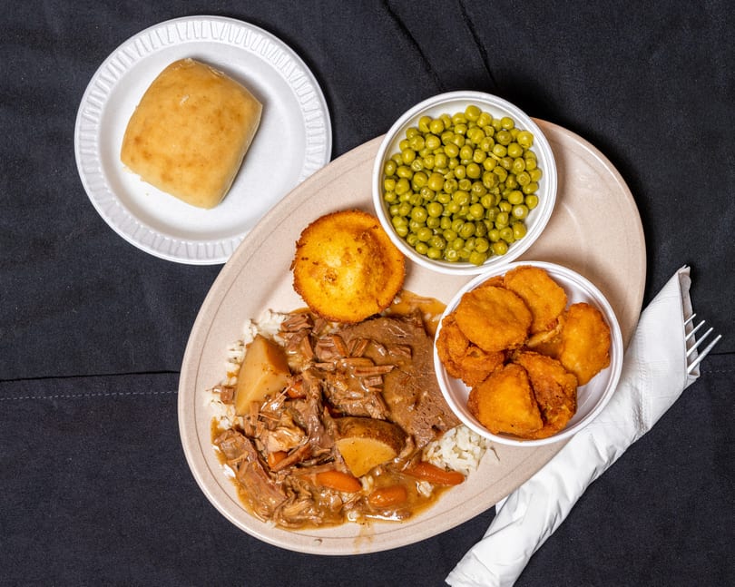 Pot roast with rice, potatoes, carrots, corn muffin, peas, and fried okra on a plate.