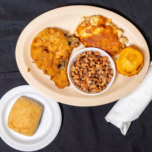 Fried chicken, macaroni and cheese, black-eyed peas, cornbread, and a roll on a black tablecloth.
