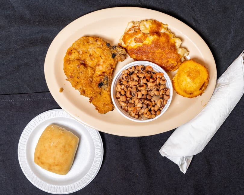 Fried chicken, macaroni and cheese, black-eyed peas, cornbread, and a roll on a black tablecloth.