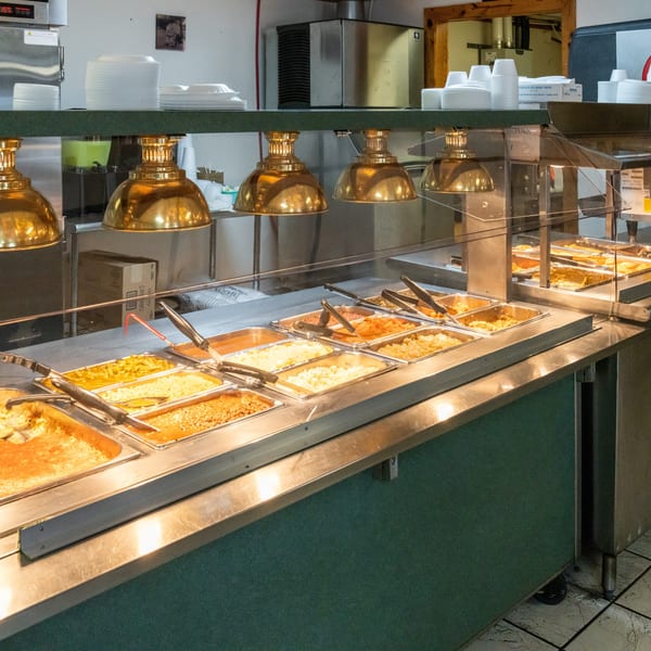 A self-serve buffet line with various hot food items in metal trays under golden heat lamps.