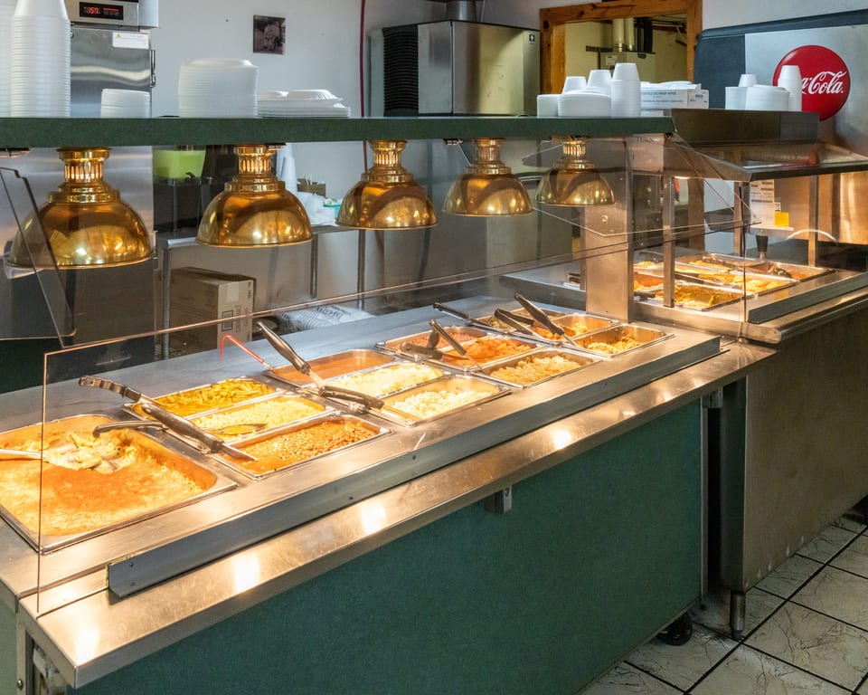 A self-serve buffet line with various hot food items in metal trays under golden heat lamps.