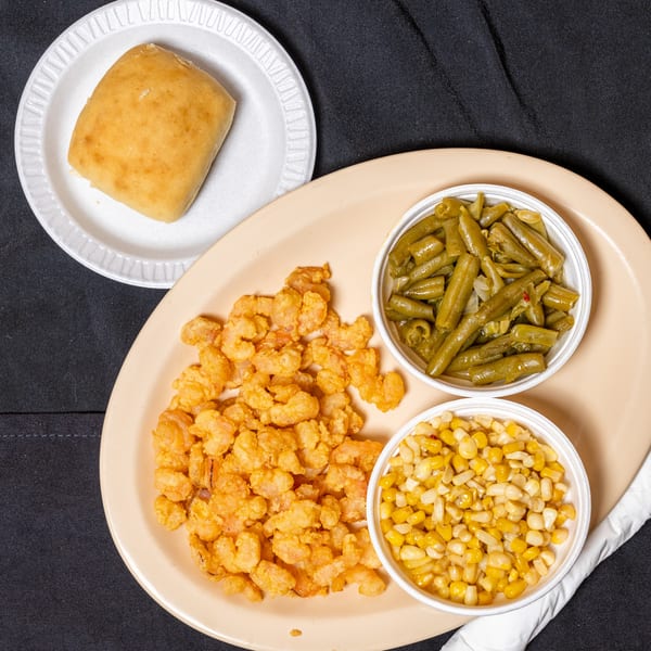 Fried shrimp with sides of green beans, corn, and a dinner roll on a black tablecloth.