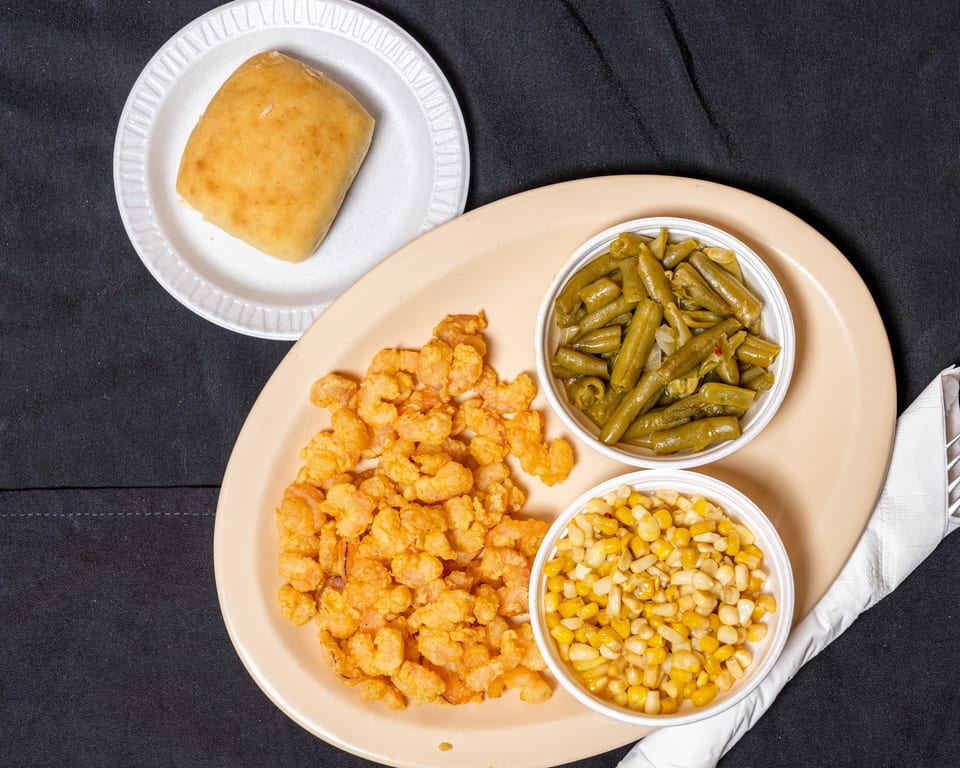 Fried shrimp with sides of green beans, corn, and a dinner roll on a black tablecloth.