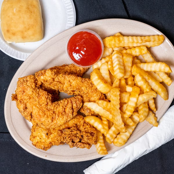 Crispy fried chicken tenders, crinkle-cut fries, ketchup, and a dinner roll on a black tablecloth.